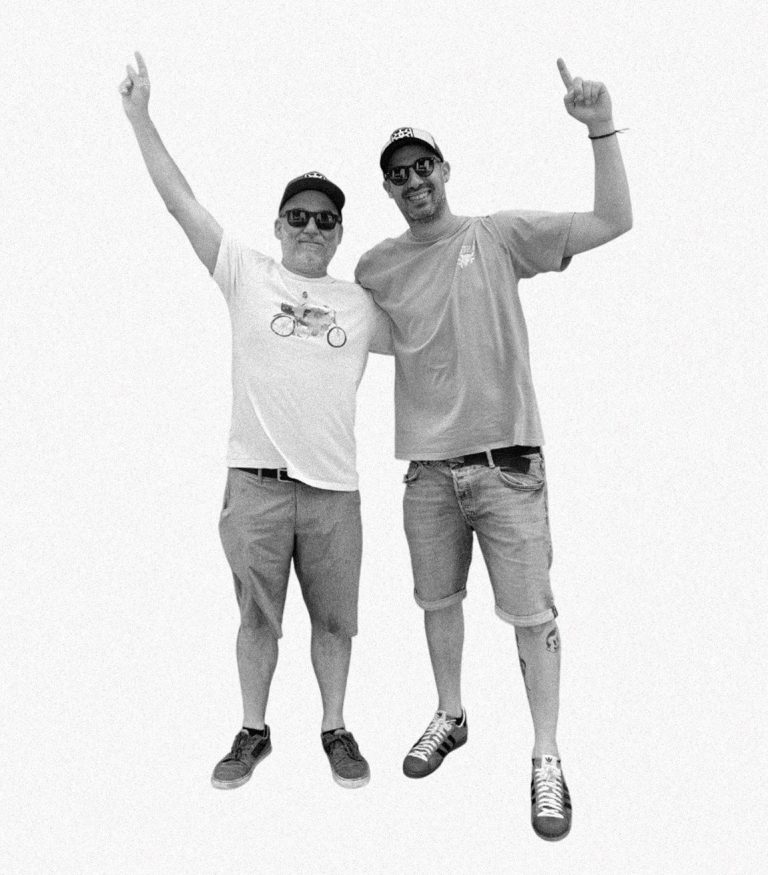 Dos hombres sonrientes levantan los brazos en señal de celebración, vestidos informalmente.