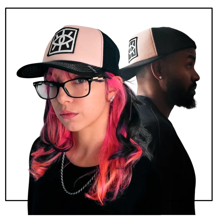 Una persona con gorra y  cabello rosa y gafas, junto a otra persona de espaldas, con gorra.